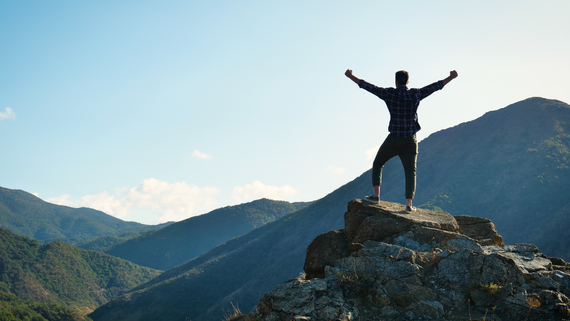 On the edge of a rocky cliff a man raises his hands to heaven as a sign of freedom